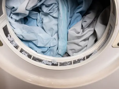 Small pumice stones and dark fleece garments inside an industrial drum mid dry-tumble cycle