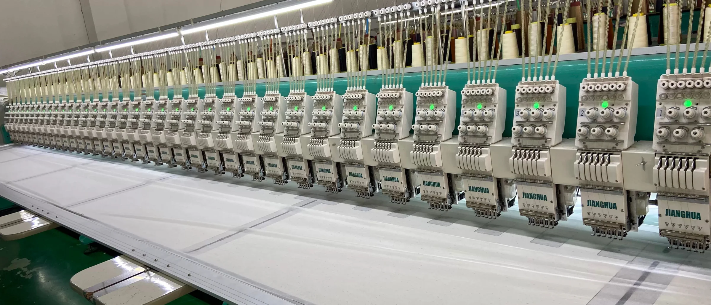 Multi-head embroidery machine mid-run stitching a logo onto garment panels