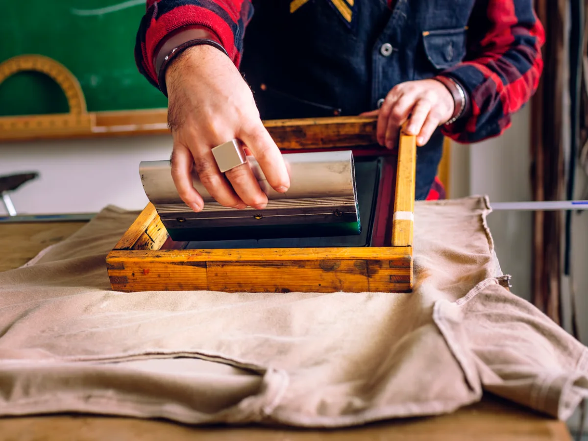 Squeegee applying ink through a screen onto a cotton T-shirt